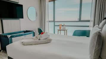 Una habitación de hotel con una cama grande, un televisor, un espejo redondo, una mesita con una computadora portátil y vista al mar.