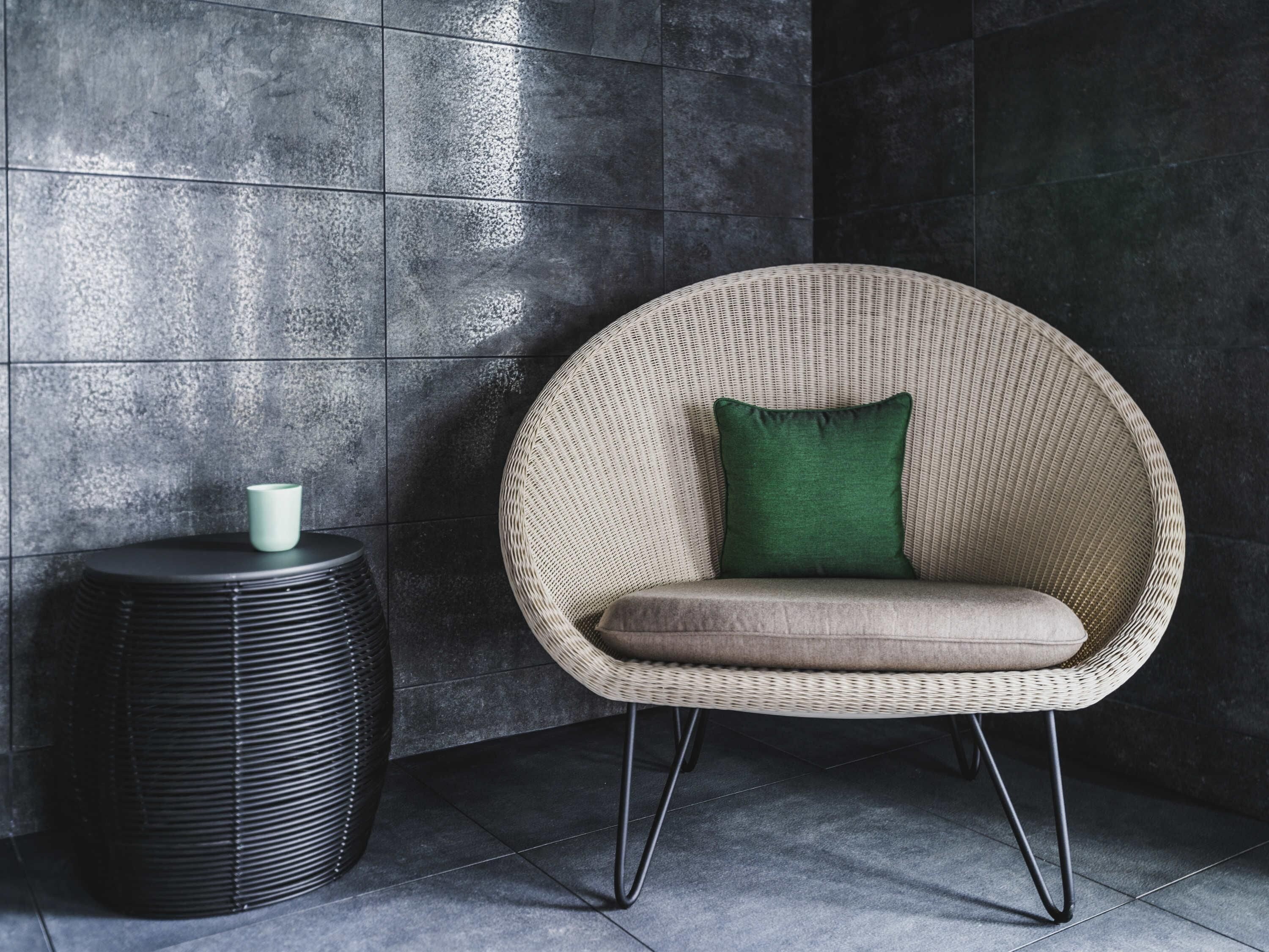 A wicker chair with a cushion and a small table beside it.