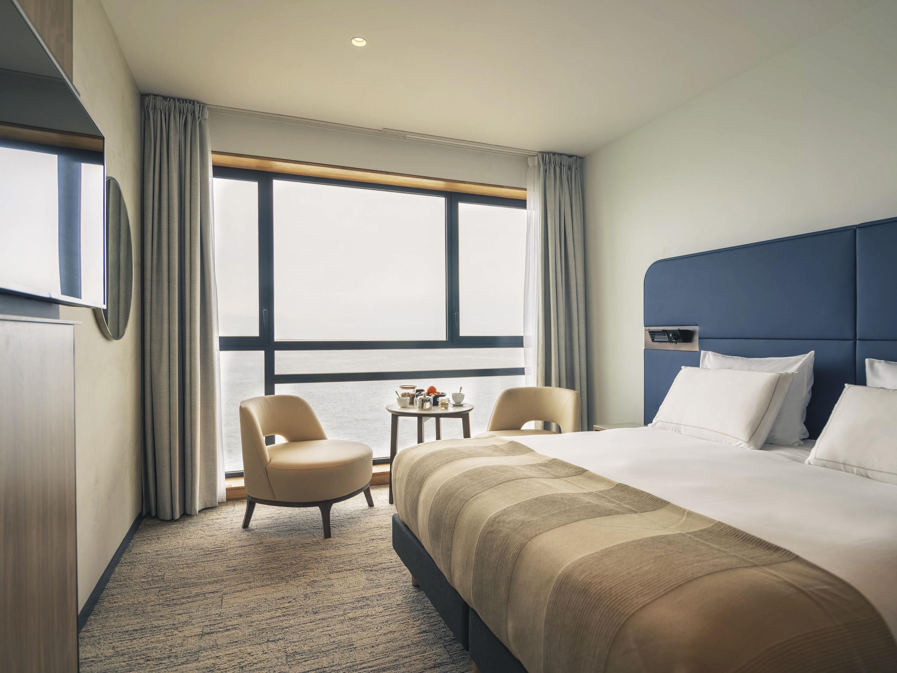 Ein Hotelzimmer mit einem großen Bett, zwei Sesseln, einem kleinen Tisch und einem Fenster mit Vorhängen.