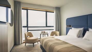 Ein Hotelzimmer mit einem großen Bett, zwei Sesseln, einem kleinen Tisch und einem Fenster mit Vorhängen.