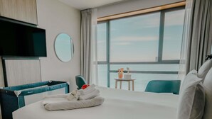 A hotel room with a large bed, a TV, a round mirror, a small table with a laptop, and a view of the sea. - Sainte-barbe Hotel Spa Le Conquet-mgallery Collect (Le Conquet)
