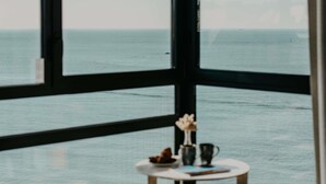 A room with a large window overlooking the sea, a small round table with a vase and a book, and a chair. - Sainte-barbe Hotel Spa Le Conquet-mgallery Collect (Le Conquet)