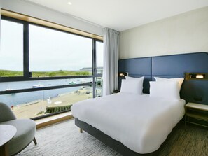 A hotel room with a large bed, a view of a body of water, and a chair. - Sainte-barbe Hotel Spa Le Conquet-mgallery Collect (Le Conquet)