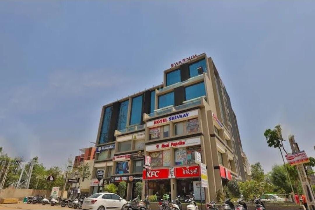 Un edificio de varios pisos con un restaurante KFC en la planta baja, un hotel llamado 'Hotel Shivaaay' en el segundo piso, y un letrero con la palabra 'Swarnim' en la parte superior.