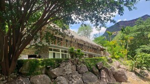 A hotel with a thatched roof, stone walls, and a view of a mountain.