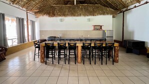 A spacious kitchen with a thatched roof, a central island with bar stools, and a tiled floor.