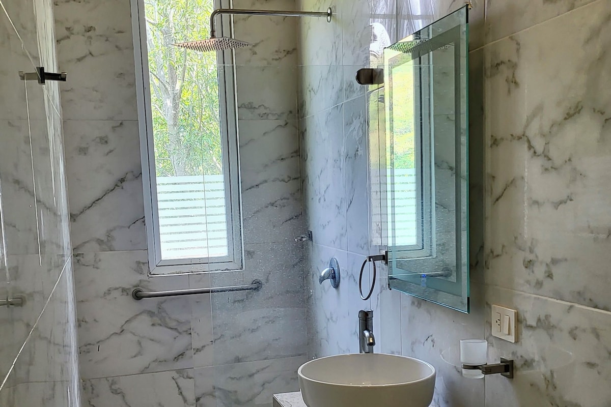 Ein Badezimmer mit Marmorwand, großem Fenster, Waschbecken und Toilette.