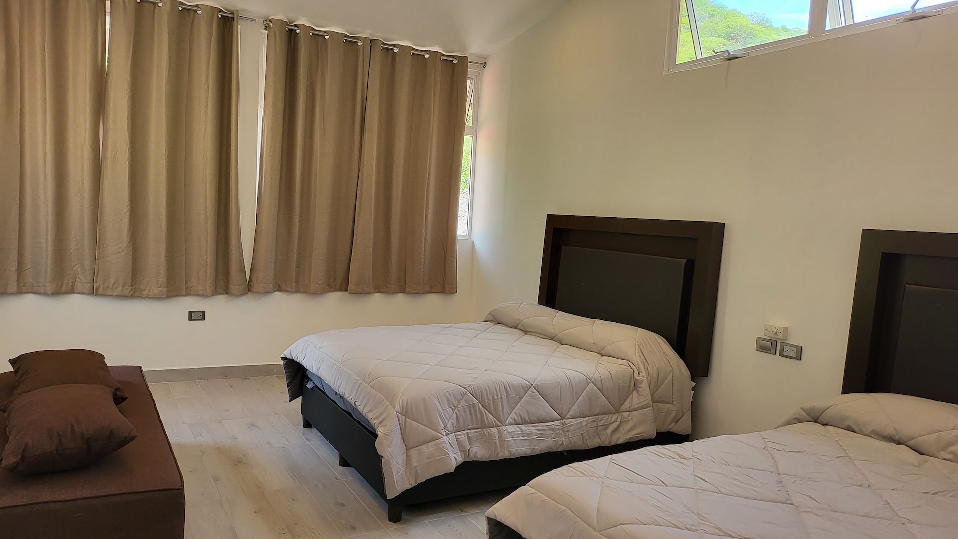 A bedroom with two beds, a sofa, and a window with curtains.