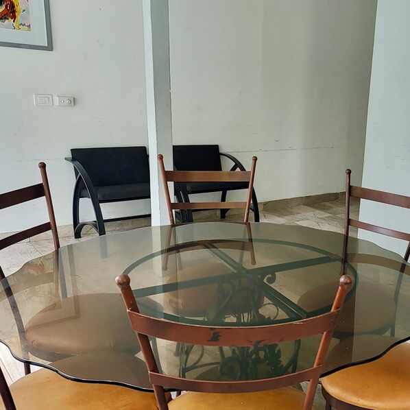 A round glass table with four wooden chairs, a white wall, and a tiled floor. - Rancho El Venado Termales (Acatic)