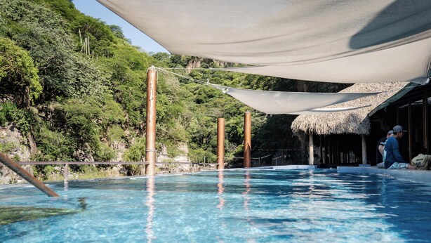 A swimming pool with a thatched-roof structure in the background.