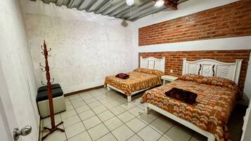 A room with two beds, a wooden coat rack, a ceiling fan, and a brick wall.