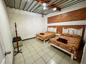 Ein Zimmer mit zwei Betten, einem Holz-Kleiderständer, einem Deckenventilator und einer Ziegelwand.