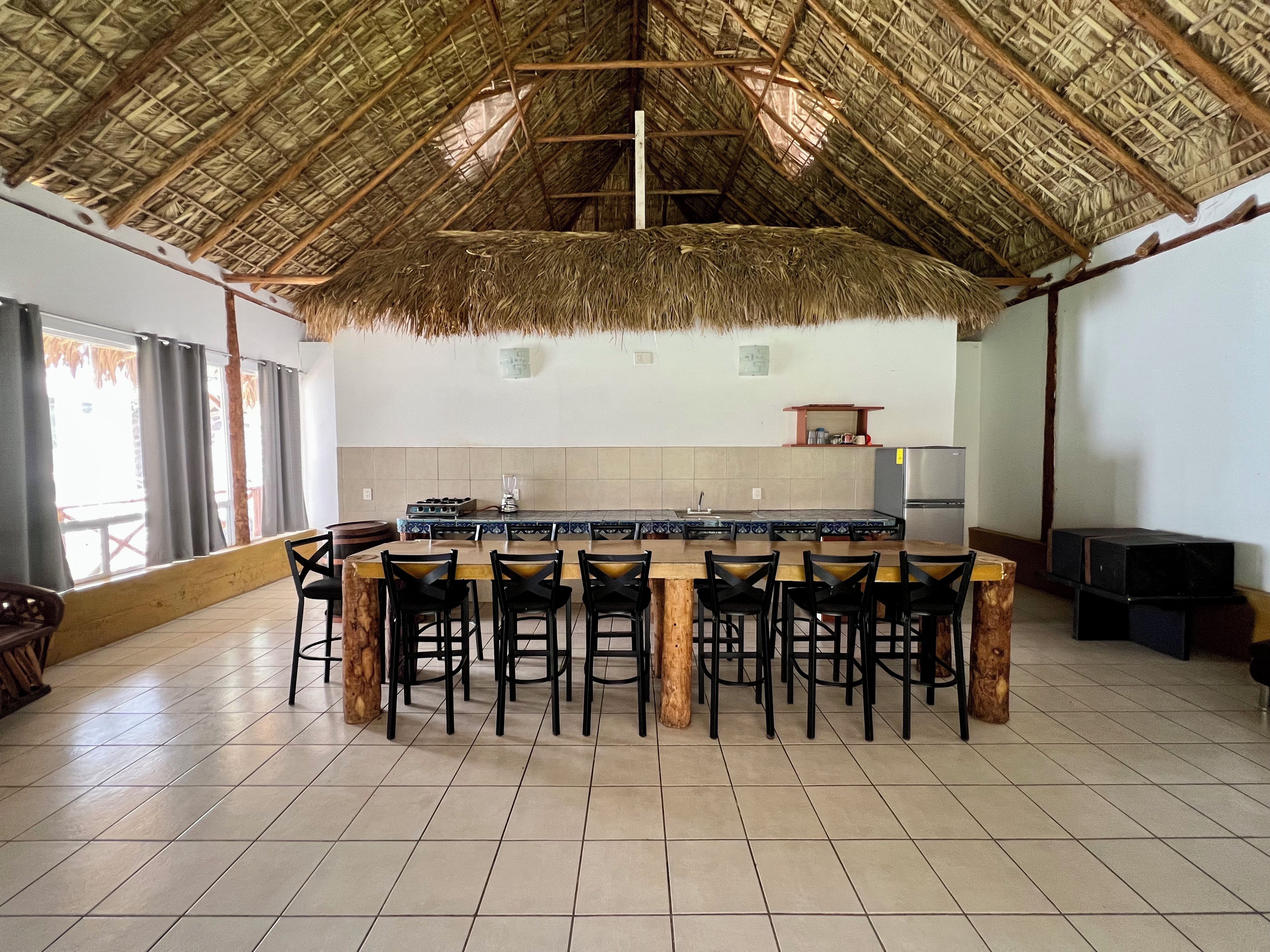 A spacious kitchen with a thatched roof, a central island with bar stools, and a tiled floor.