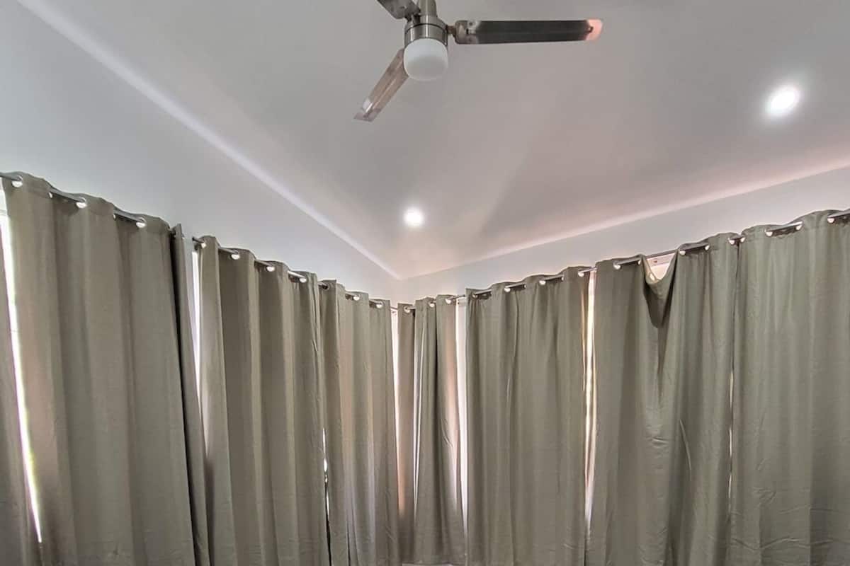 Un dormitorio con dos camas, un ventilador de techo y cortinas.