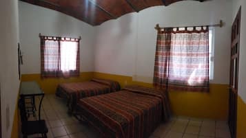 A room with two beds, a small table, and two windows with patterned curtains.