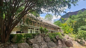 Hotel amb teulada de palla, parets de pedra i vistes a la muntanya.
