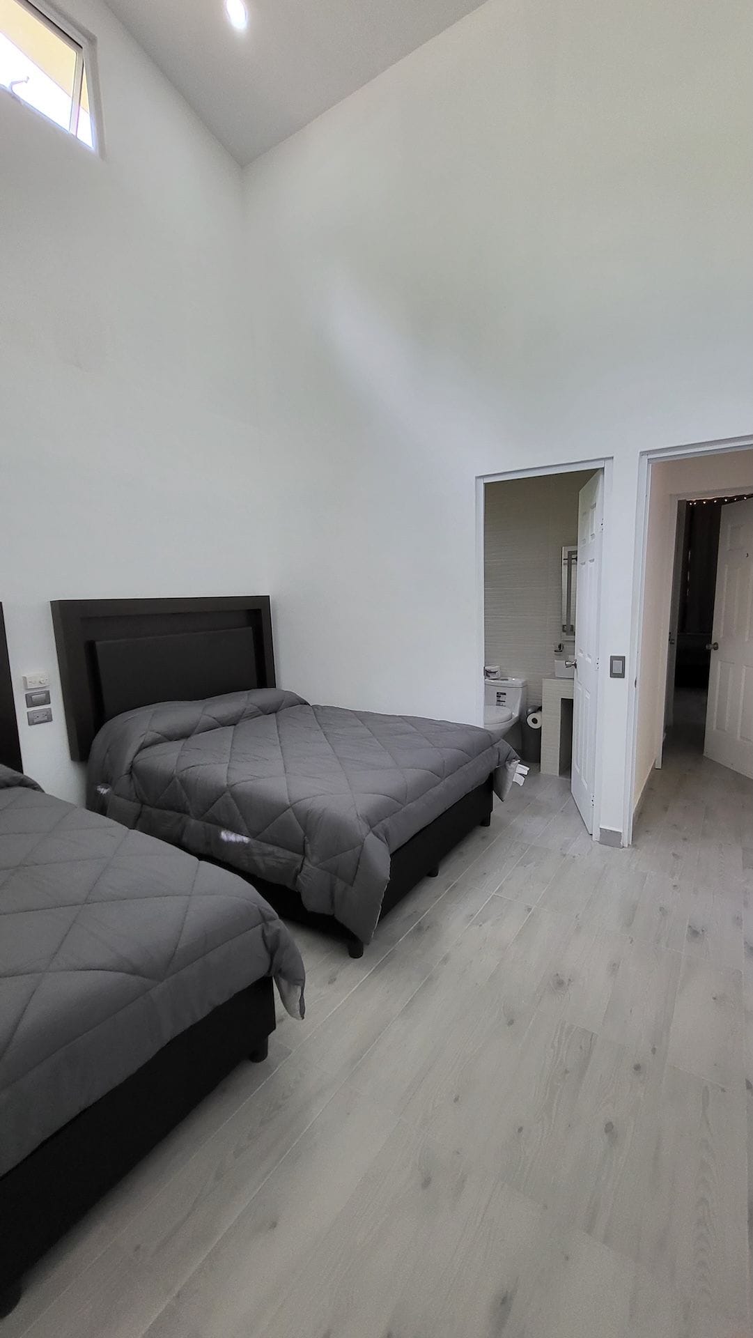 Un dormitorio con dos camas, un baño y un pasillo.
