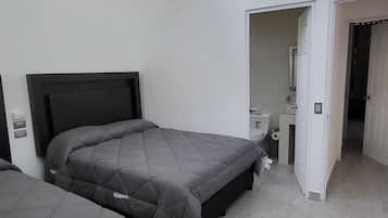 Un dormitorio con dos camas, un baño y un pasillo.