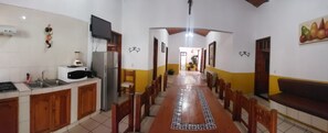 A dining area with a long wooden table, chairs, a kitchen area with a microwave, and a television on the wall. - Rancho El Venado Termales (Acatic)