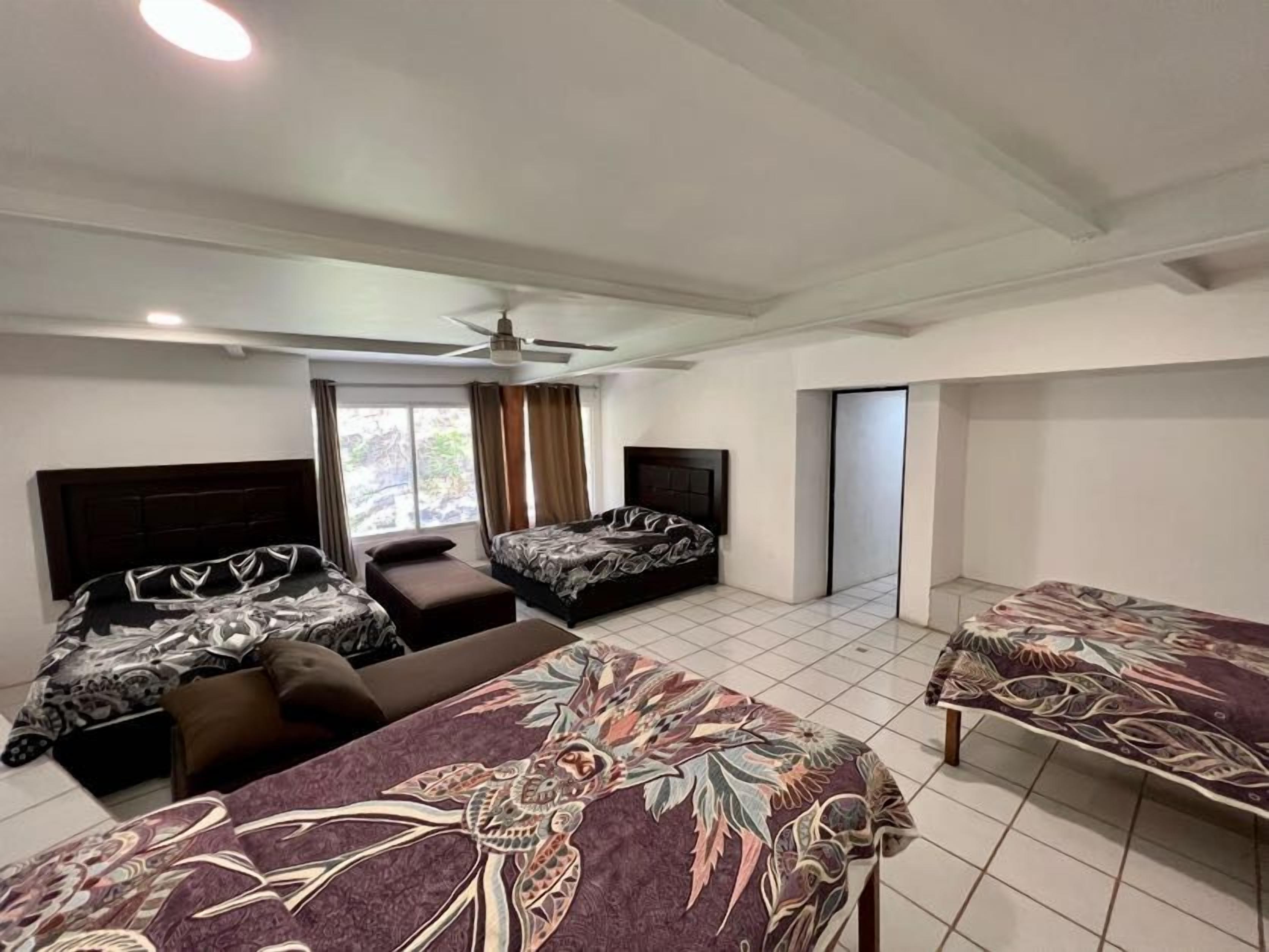 Habitación de hotel con dos camas, un sofá, ventilador de techo y ventana con cortinas.