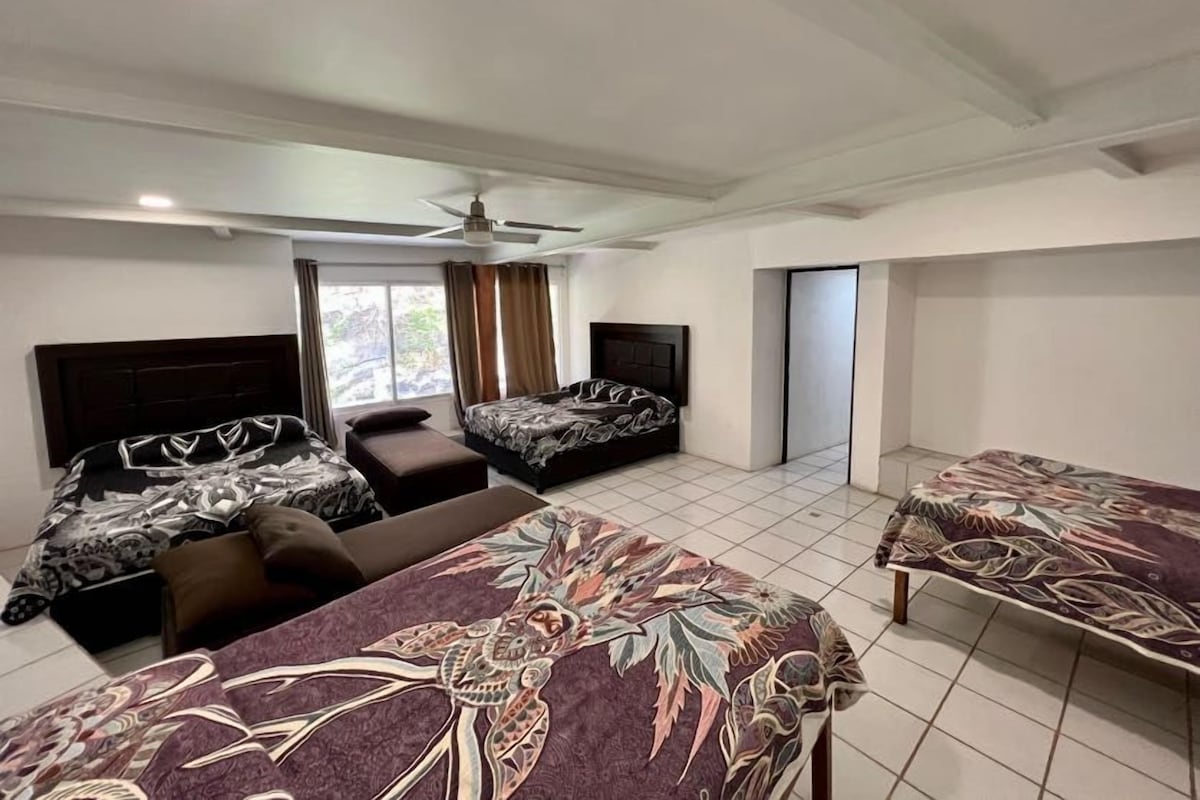 Ein Hotelzimmer mit zwei Betten, einem Sofa, einem Deckenventilator und einem Fenster mit Vorhängen.