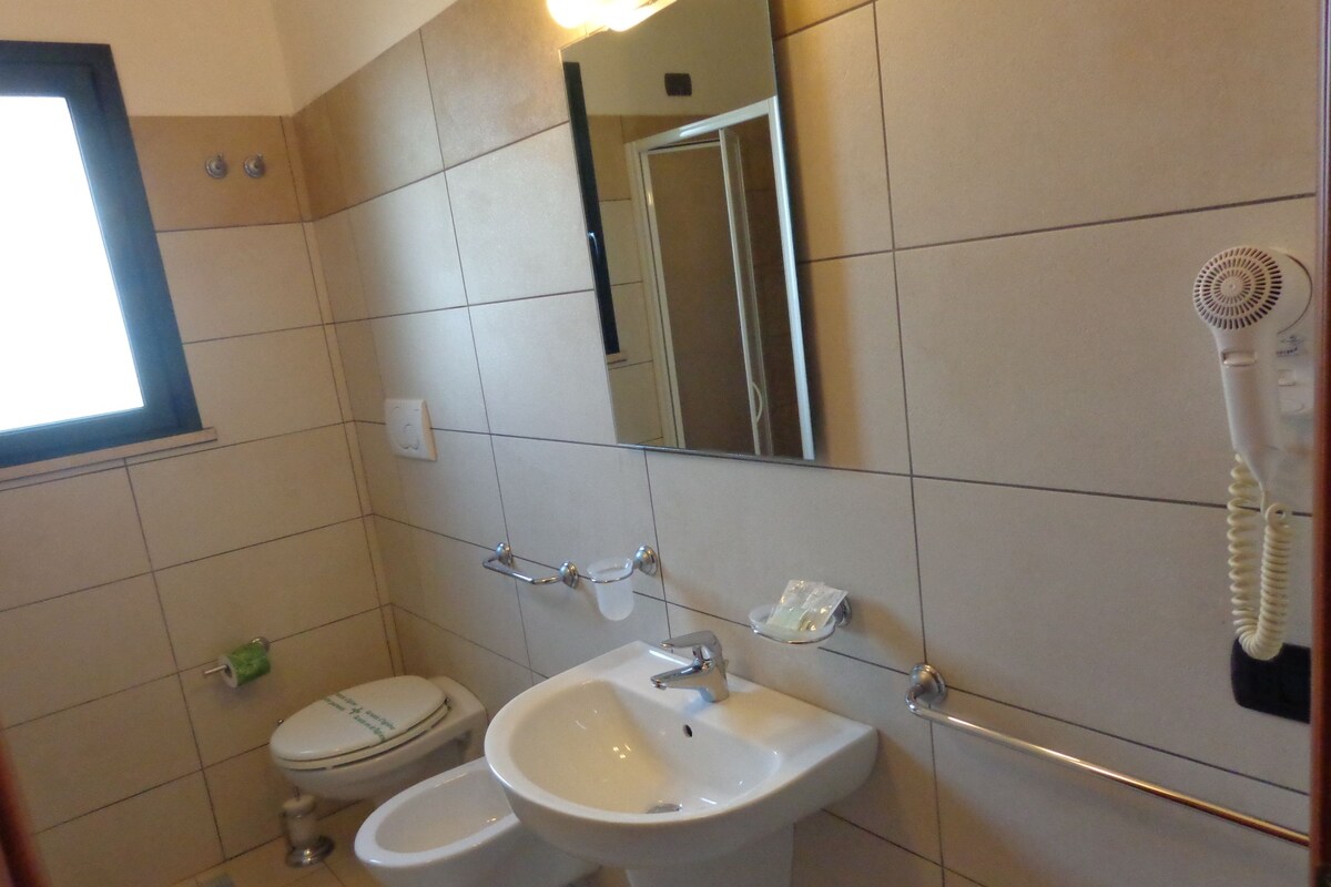 A bathroom with a toilet, bidet, sink, and a hairdryer mounted on the wall.