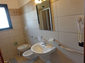 A bathroom with a toilet, bidet, sink, and a hairdryer mounted on the wall.