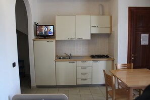 A compact kitchen with a TV, a sink, cabinets, and a dining area. - Residence Alimini Blu (Otranto)