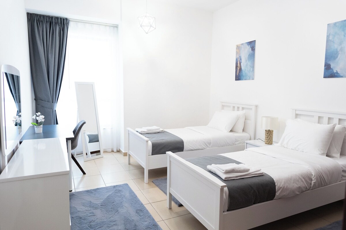 Ein Hotelzimmer mit zwei Betten, einem Schreibtisch, einem Stuhl und Bildern an den Wänden.