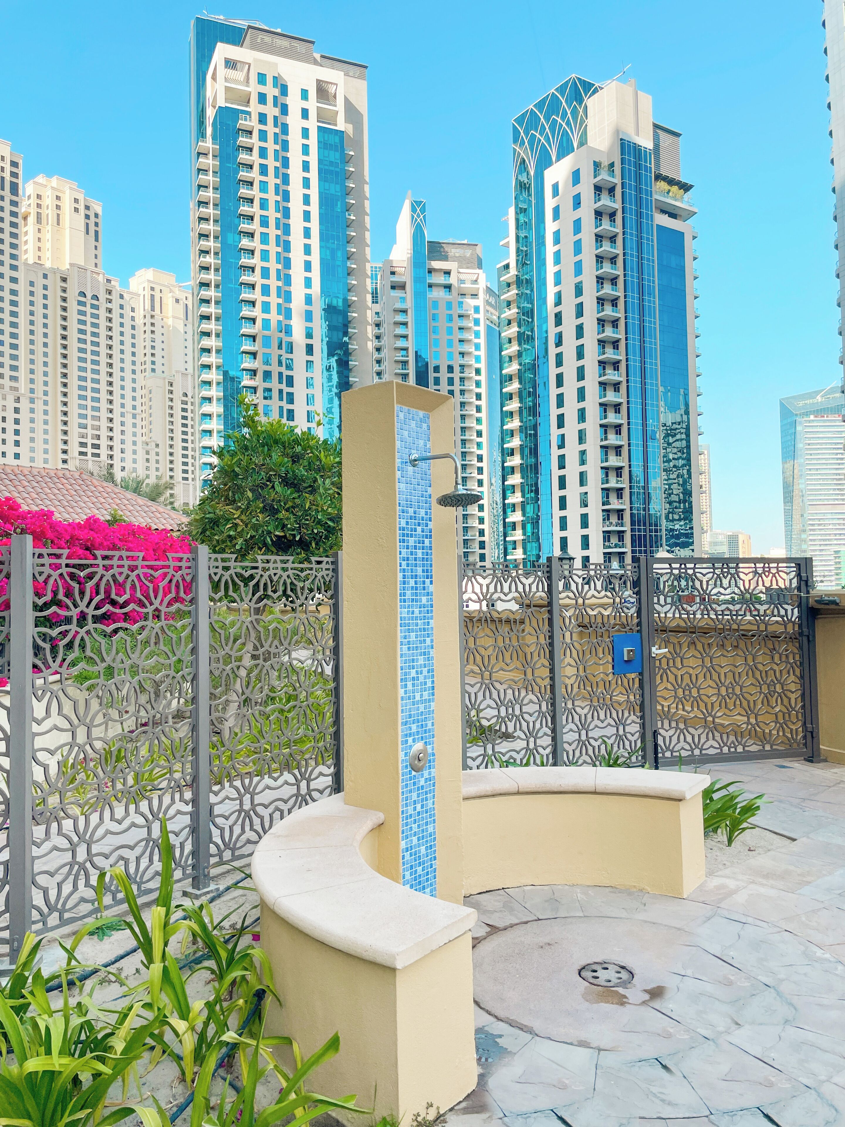 A modern urban setting with high-rise buildings, a decorative metal fence, and a tiled column.