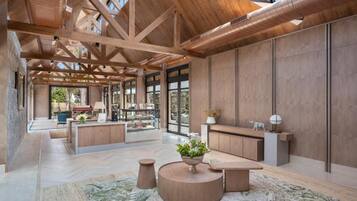 A spacious interior with a high ceiling, wooden beams, a central seating area with a round table, and a view through large windows.
