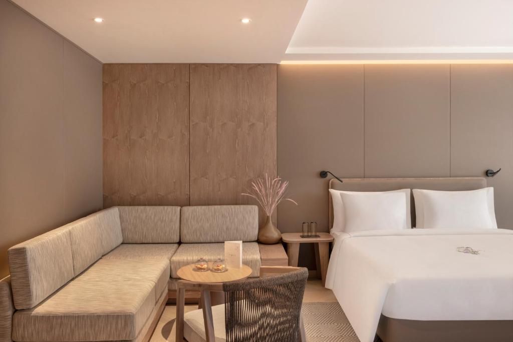 A modern hotel room with a sofa, a small round table, a chair, a bed, and a nightstand.