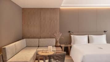 A modern hotel room with a sofa, a small round table, a chair, a bed, and a nightstand.