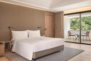 A modern hotel room with a large bed, a small bedside table, a nightstand, a sliding glass door to a balcony with outdoor furniture. - Zana in The Wild, Dhikuli (Ramnagar)