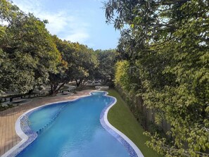 A swimming pool with a curved edge, surrounded by a paved deck and lush greenery.