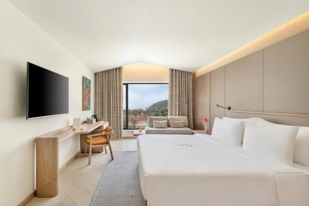 Una habitación de hotel con cama, escritorio, silla, televisor y vistas al exterior.