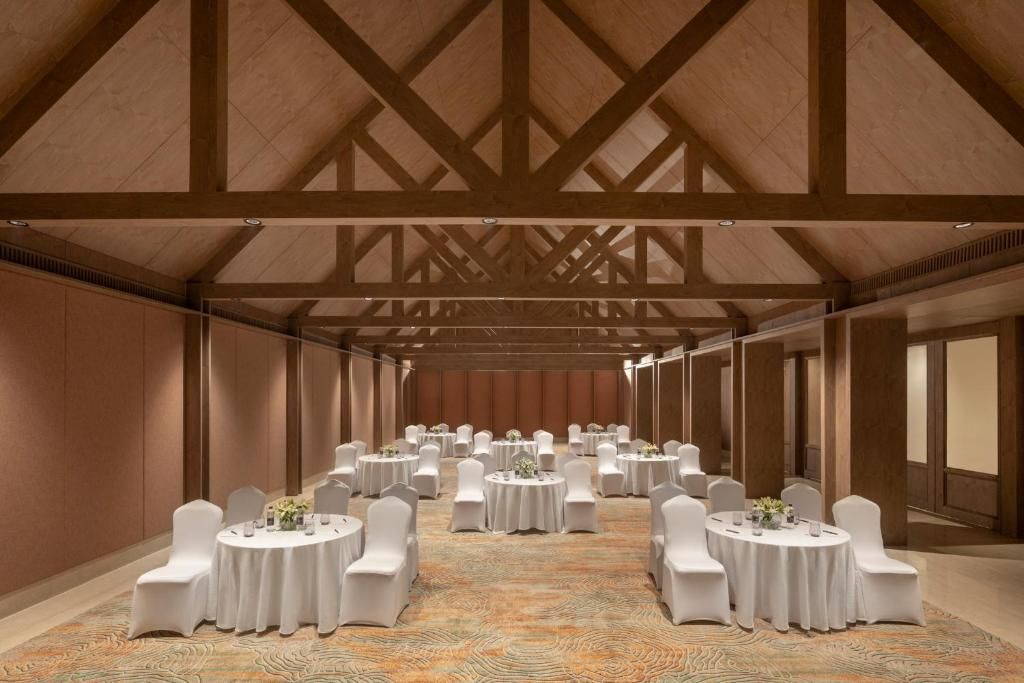 A banquet hall with round tables and white chairs, wooden beams on the ceiling, and a patterned carpet.