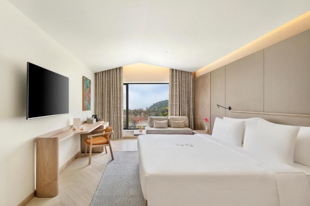 A hotel room with a bed, a desk, a chair, a TV, and a view of the outdoors.