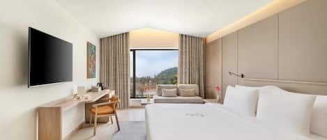 A hotel room with a bed, a desk, a chair, a TV, and a view of the outdoors.