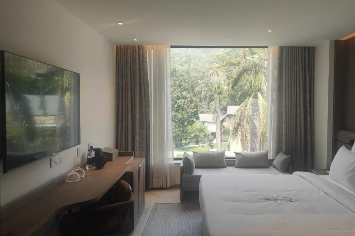 Ein Hotelzimmer mit einem großen Bett, einem Schreibtisch, einem Fernseher und einem Fenster mit Blick auf Grünflächen.