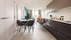 A modern kitchen with dark cabinetry, a dining area with chairs, and a view to the living room. - Charles Hope Apartments - Leeds (Leeds)
