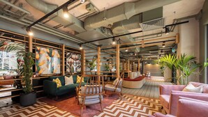 A modern interior with a green sofa, wooden chairs, a patterned rug, and potted plants. - Charles Hope Apartments - Leeds (Leeds)