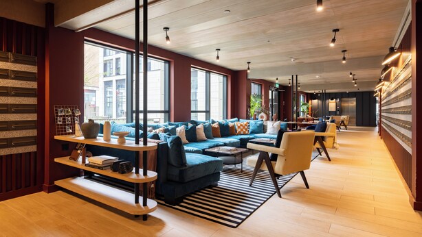 A modern living room with a blue sectional sofa, wooden shelves, and a striped rug. - Charles Hope Apartments - Leeds (Leeds)