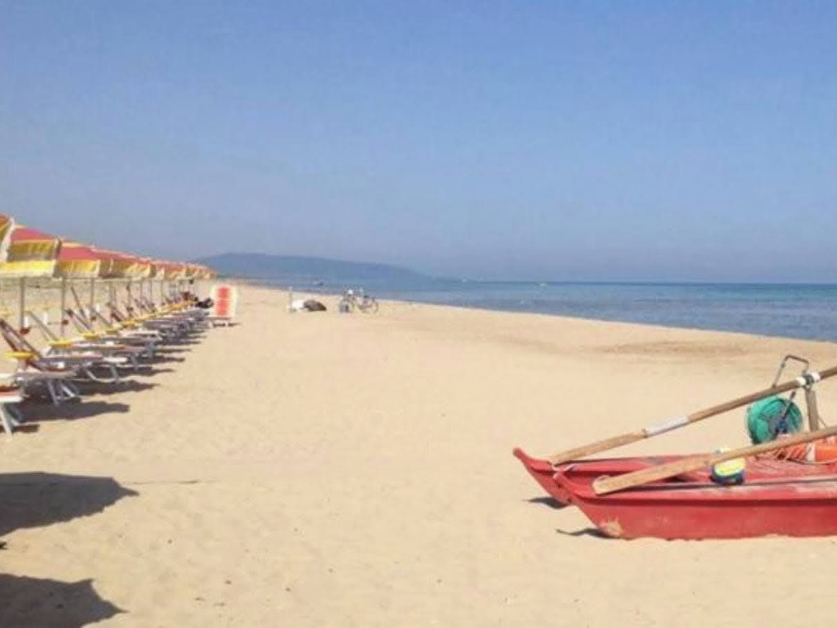 A beach with rows of sun loungers and a red boat.