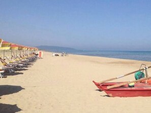 A beach with rows of sun loungers and a red boat.