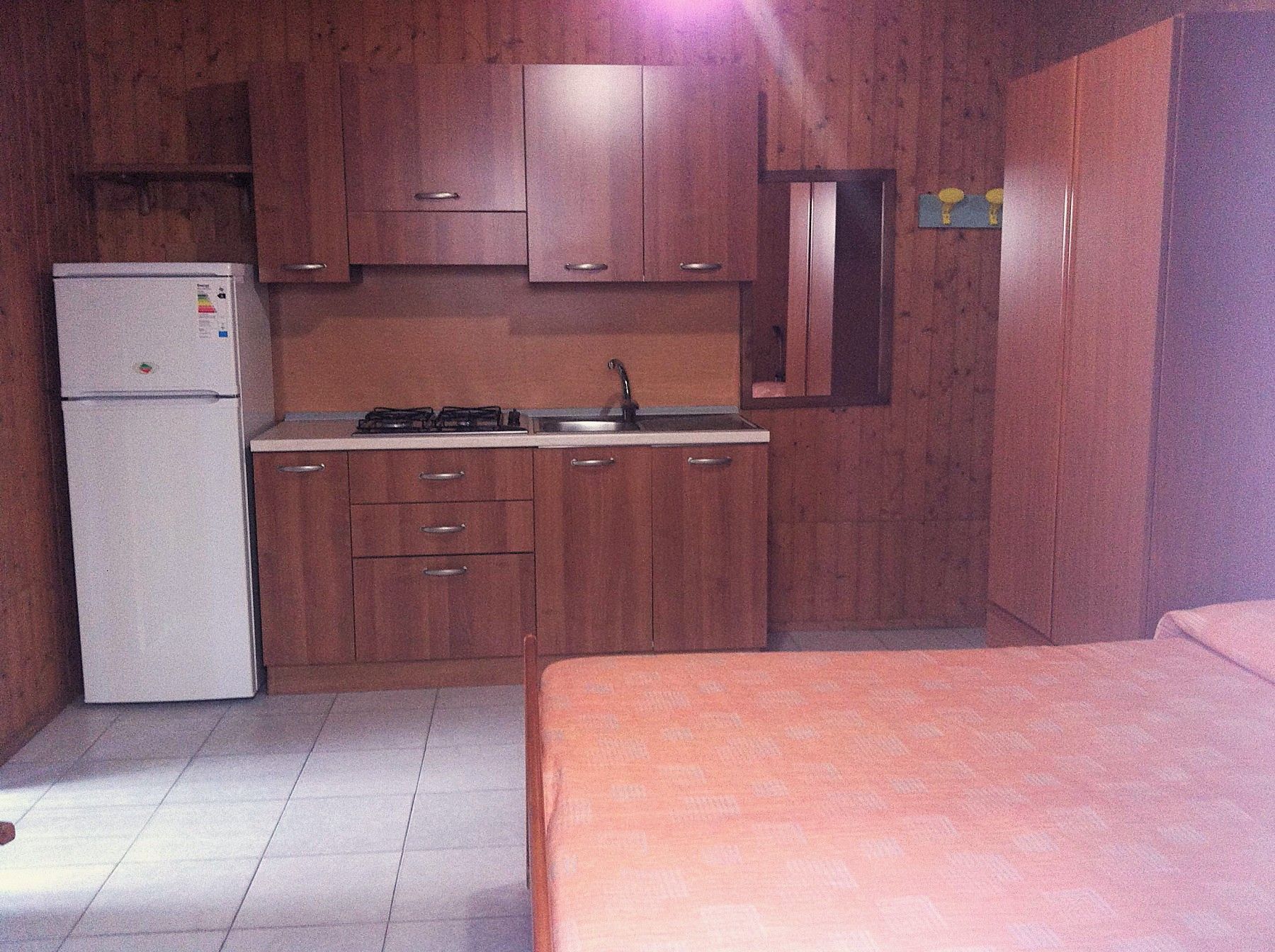 A compact kitchen with a refrigerator, stove, sink, and wooden cabinets.