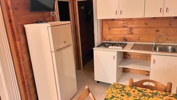 A compact kitchen with a refrigerator, stove, sink, and a television mounted above the counter.