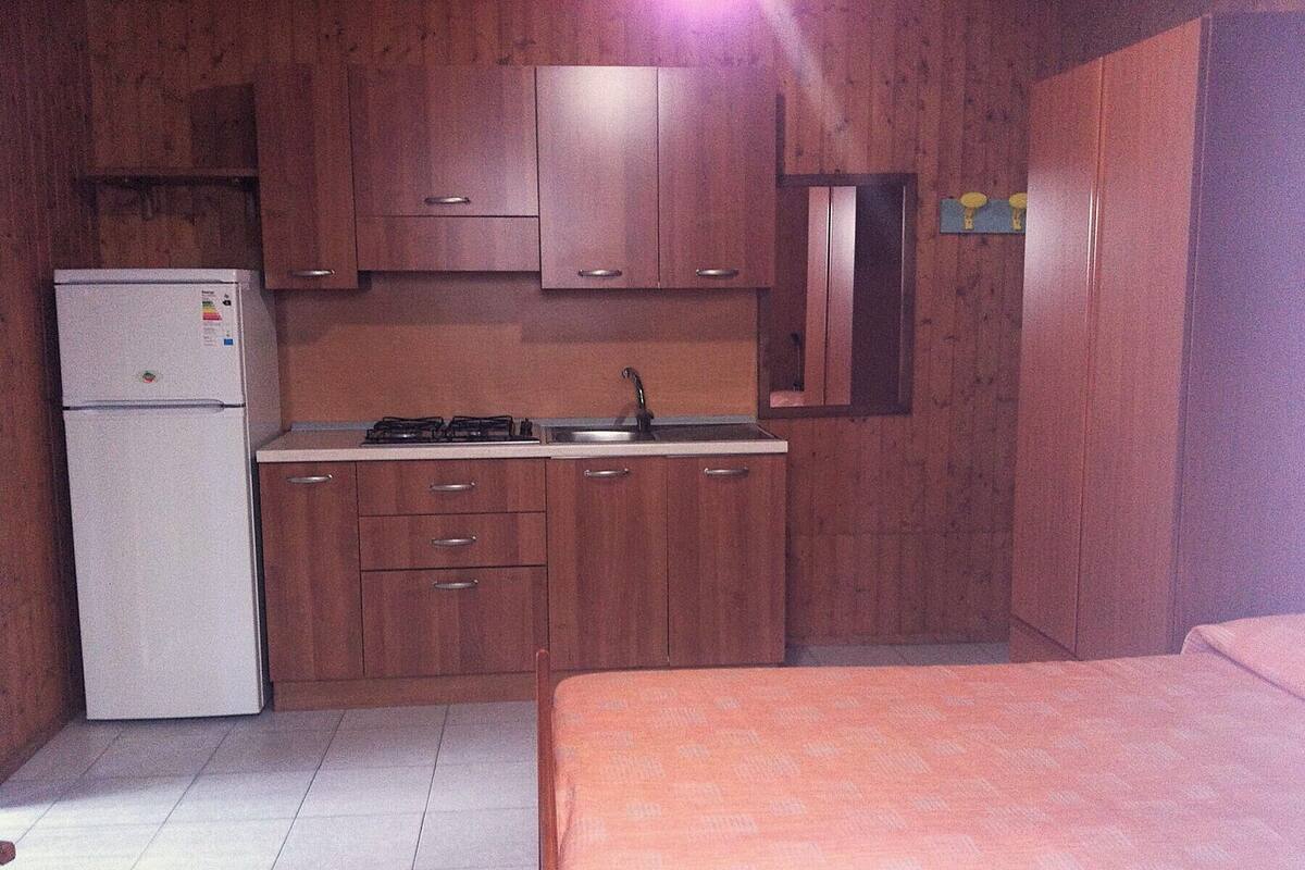 Una cocina compacta con refrigerador, estufa, lavamanos y armarios de madera.