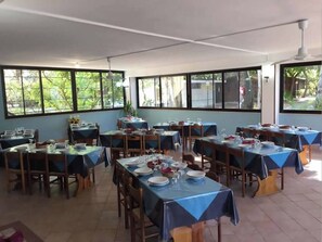 A dining area with multiple tables set for meals, large windows, and a ceiling fan.