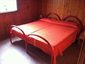 A single bed with a red bedspread in a room with wooden walls and a window.